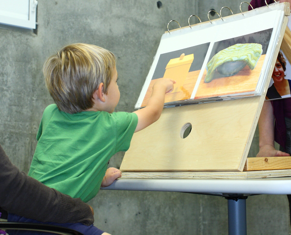 A young boy is pointing towards a picture of a yellow box.